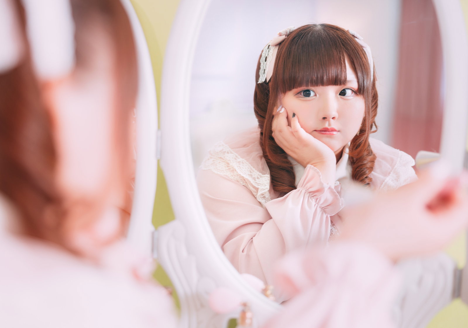 ピンク色のトップスとツインテール姿の女性がミラーに映った自分を見つめている［モデル：あづき］