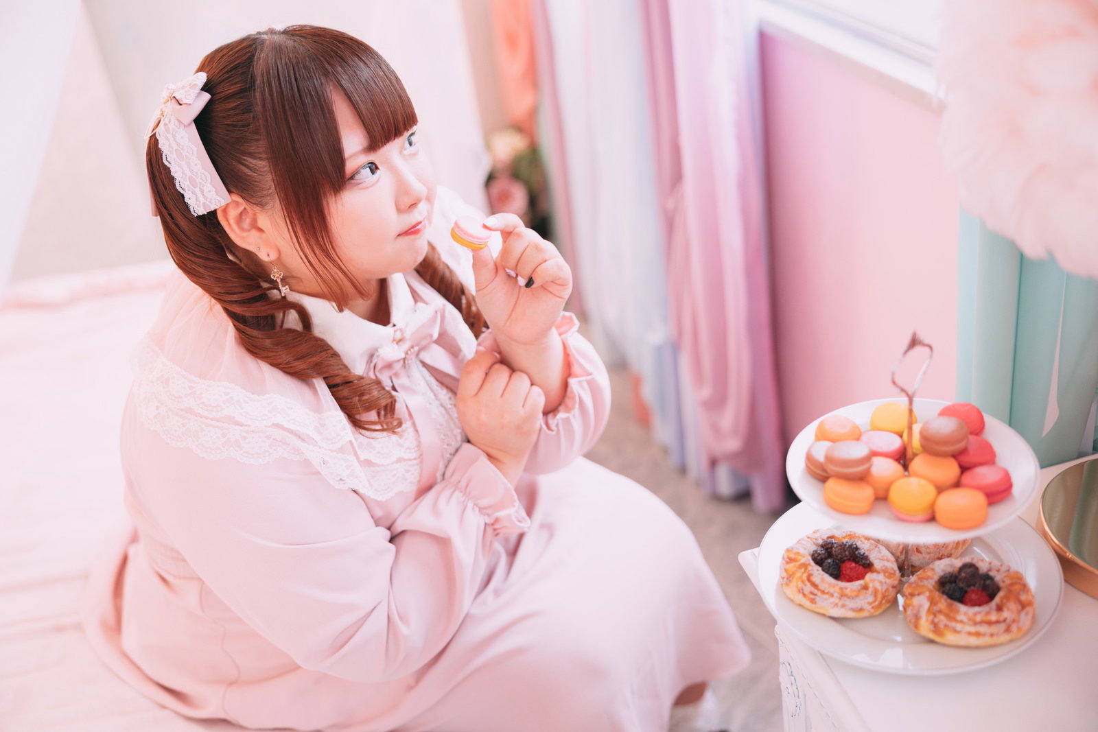 ピンクのワンピースを着てマカロンを食べるツインテール女性［モデル：あづき］