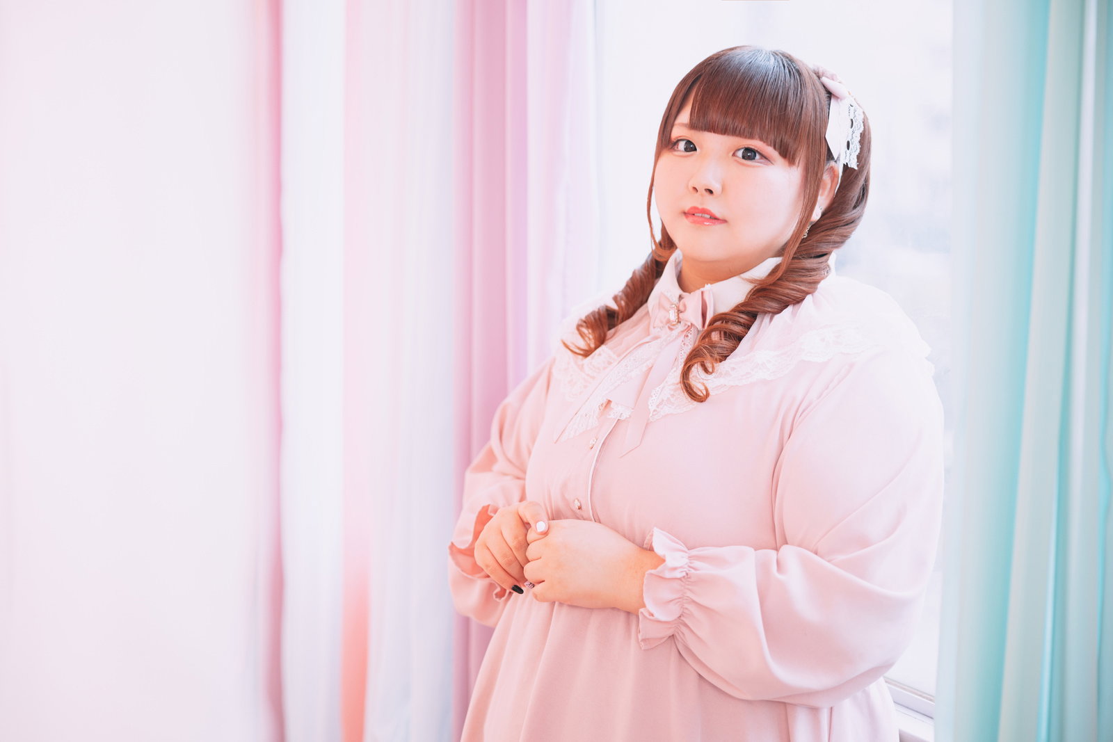 ピンク衣装のツインテール女性が窓際で微笑む［モデル：あづき］