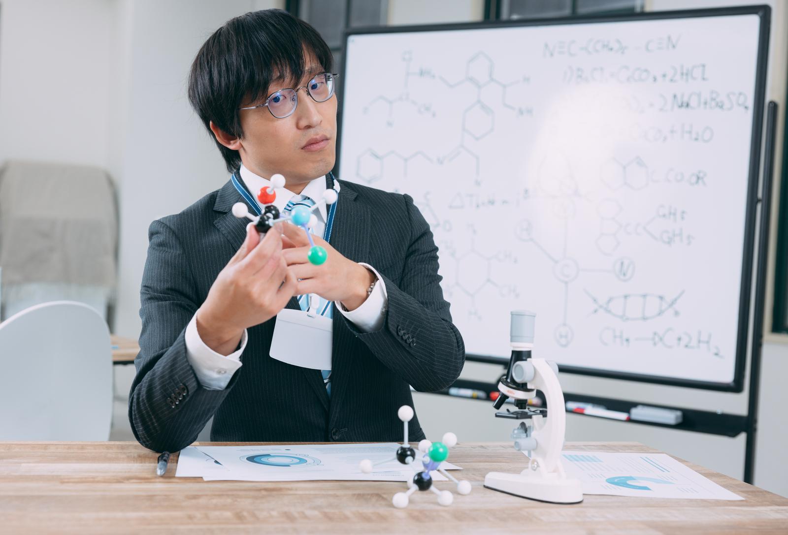 分子模型を手に持つスーツ姿の研究者［モデル：あづま］