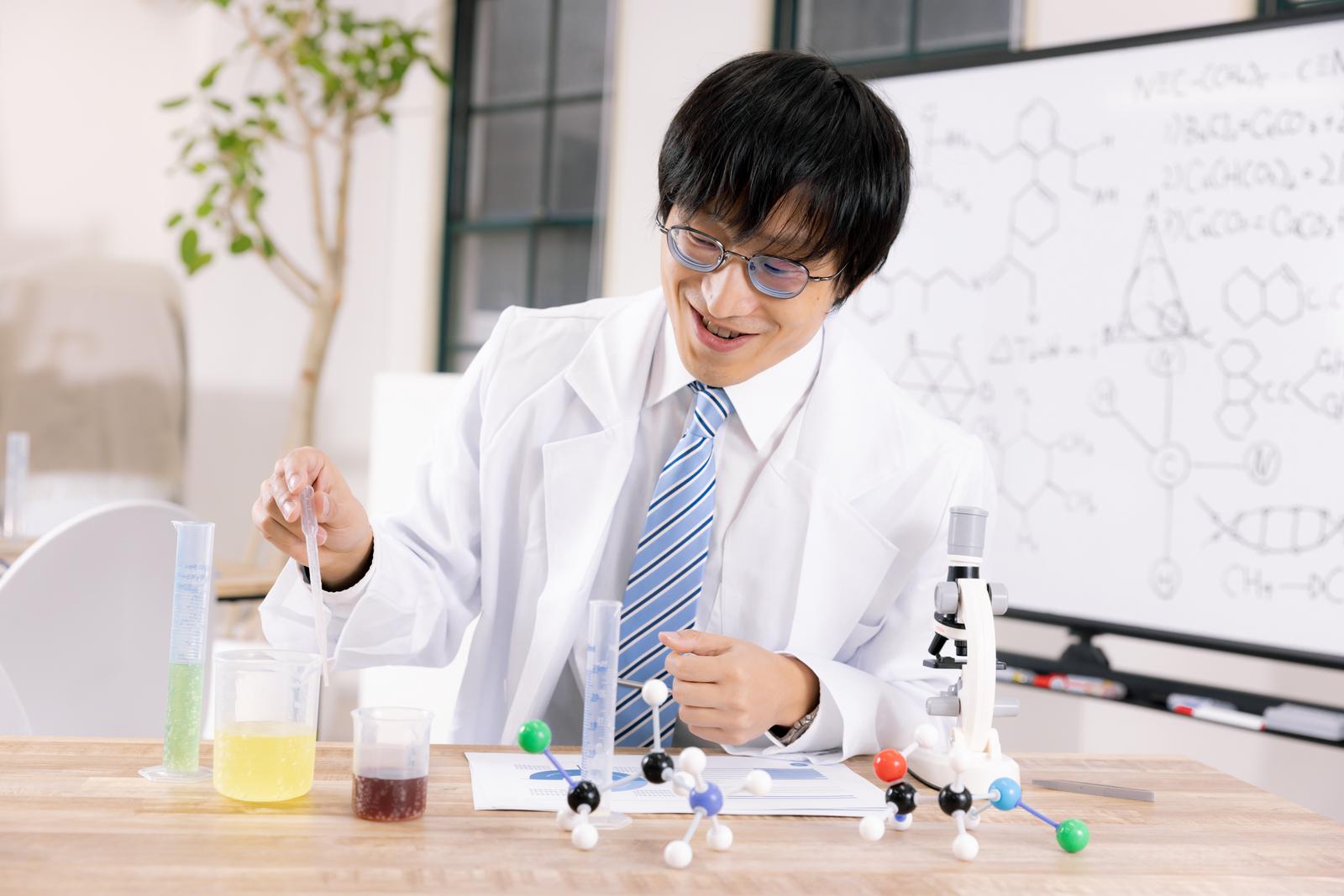 白衣を着た眼鏡の男性が試験管を持ち薄く笑みを浮かべながら実験を行う［モデル：あづま］