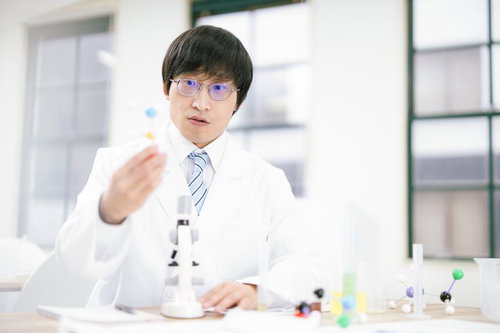 研究中に何か発見した白衣姿の男性科学者が右手を上げて説明している