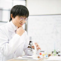 研究室で顕微鏡を操作しながら考える科学者の男性の写真