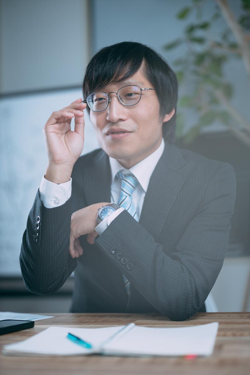 眼鏡を押し上げながら指摘する紺シャツのビジネスマン［モデル：あづま］