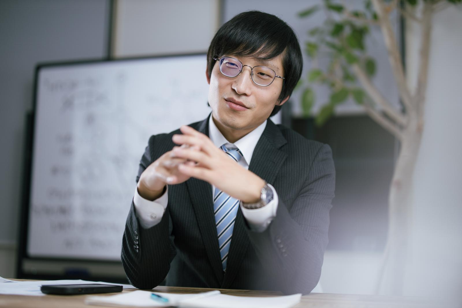 オフィスで説明するスーツ姿の男性［モデル：あづま］