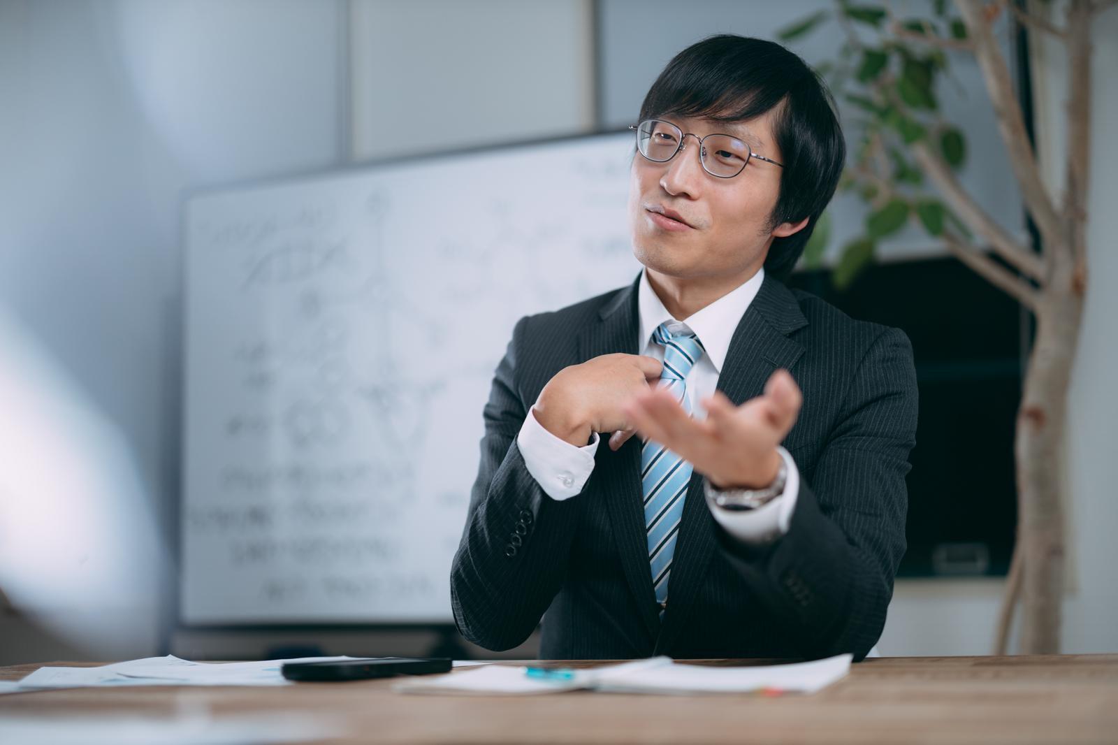 会議室でジェスチャーしながら主張する男性［モデル：あづま］