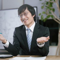 何を言ってるかさっぱりわかりませんよと机で説明する眼鏡の男性の写真