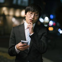 夜間の街中でスマートフォンをチェックする眼鏡の男性の写真