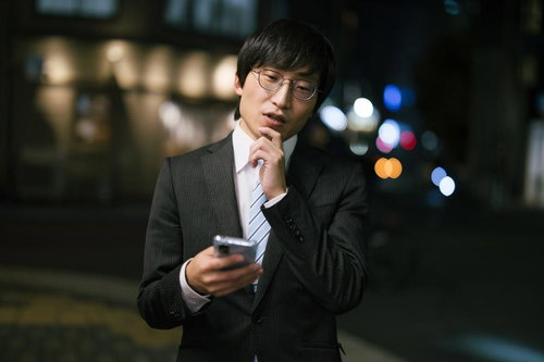 夜間の街中でスマートフォンをチェックする眼鏡の男性