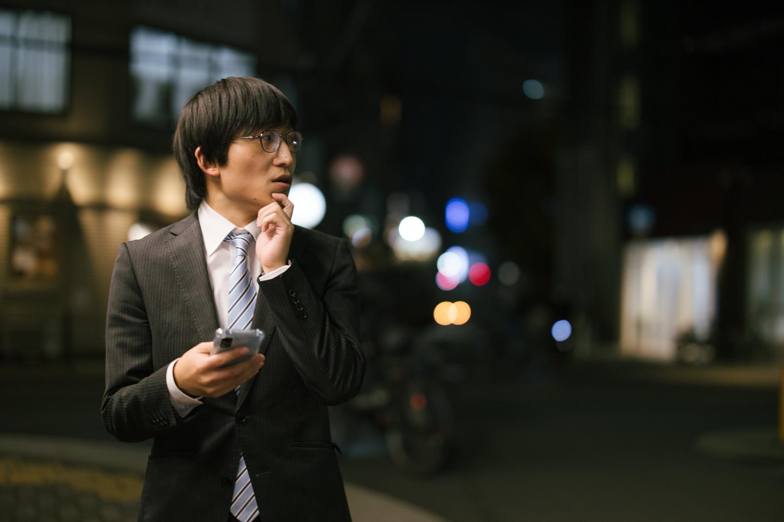 スマートフォンでマップを見ながら待ち合わせ場所を探す不安そうな男性［モデル：あづま］