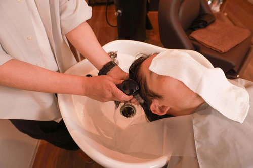 美容室で洗髪をする男性、白いシャンプー台でヘアケア施術を受ける