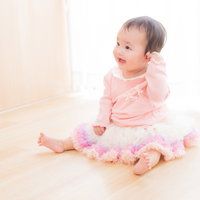 ピンク色の服を着てお座りご満悦のベビー、両手を広げ嬉しそうな表情の写真