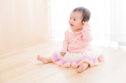 ピンク色の服を着てお座りご満悦のベビー、両手を広げ嬉しそうな表情