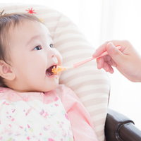 ピンクの服を着た赤ちゃんが大きなお口をあけて離乳食をあーんの写真
