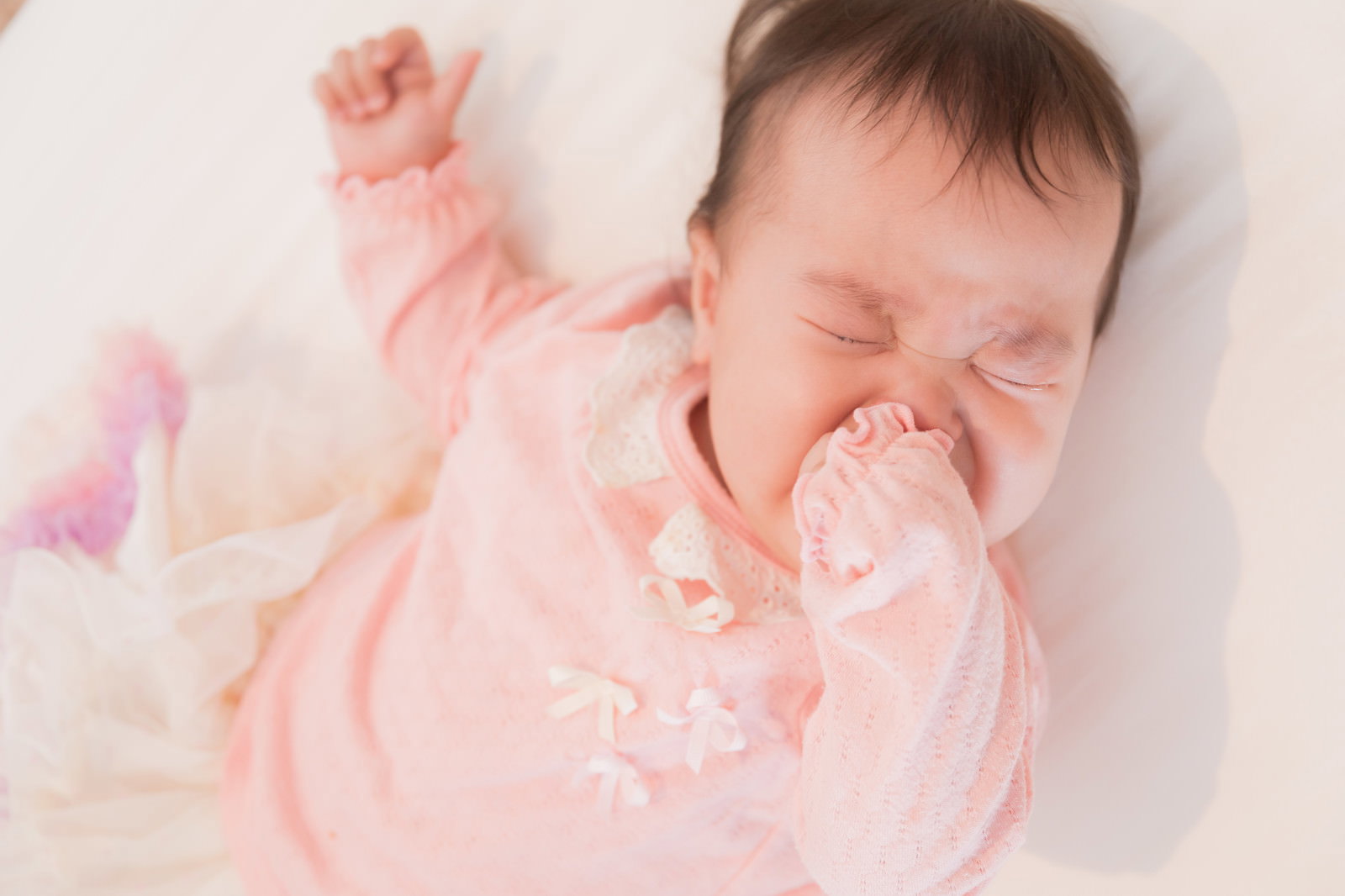 ピンクの服を着た赤ちゃんが白いタオルの上で涙を流しながらギャン泣きしている［モデル：めぐな］