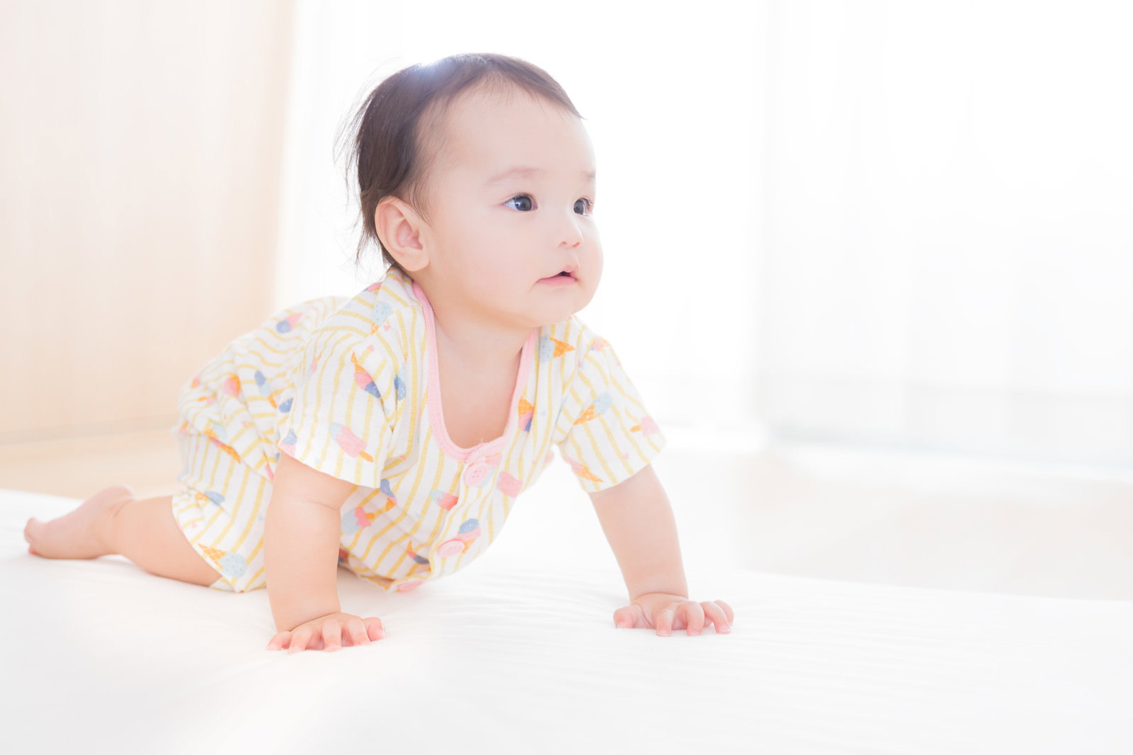 白い服を着た赤ちゃんがハイハイしている様子［モデル：めぐな］