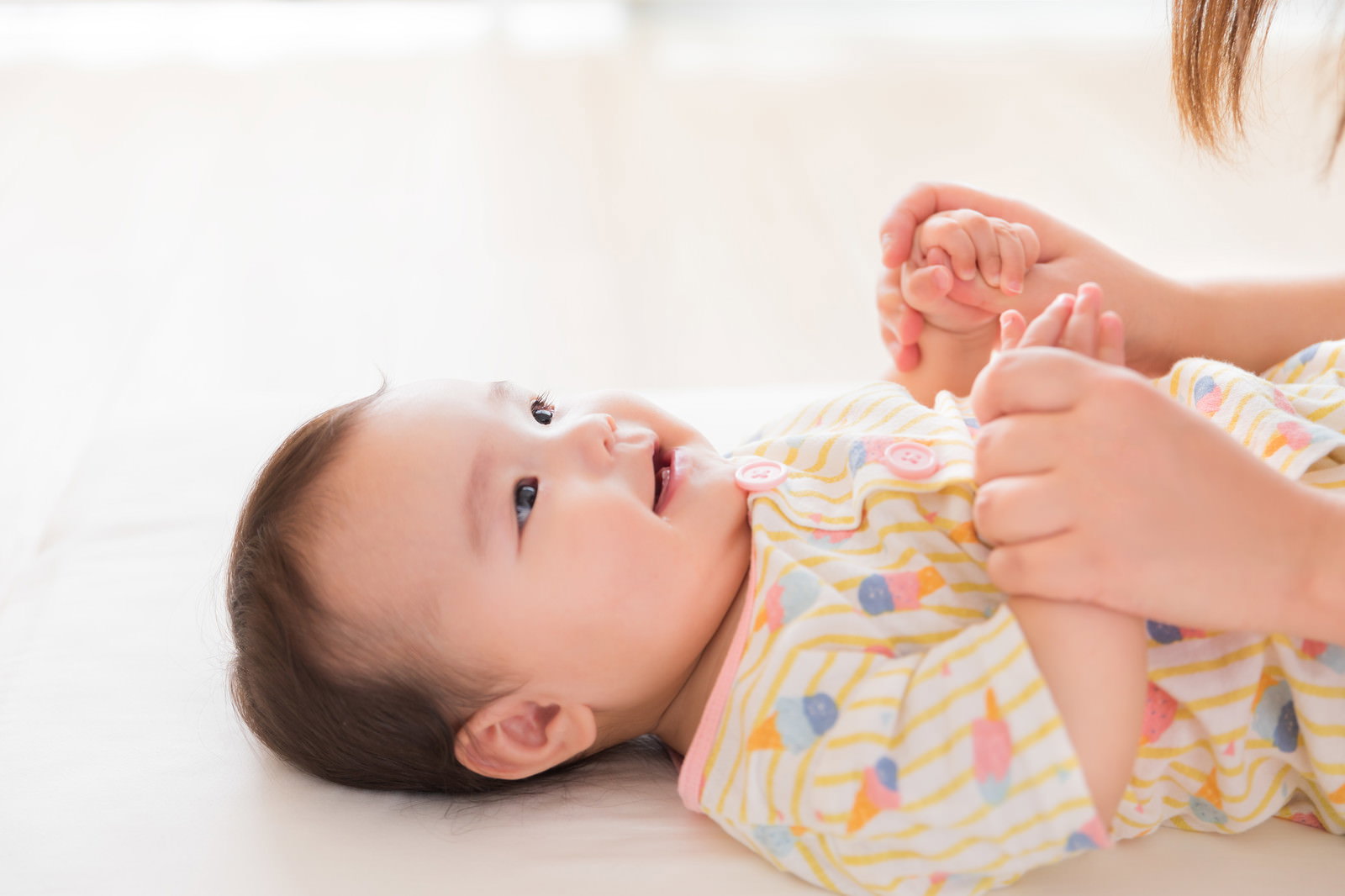 笑顔を浮かべる赤ちゃんに優しく手を添えるママの愛情あふれるスキンシップの様子［モデル：めぐな］