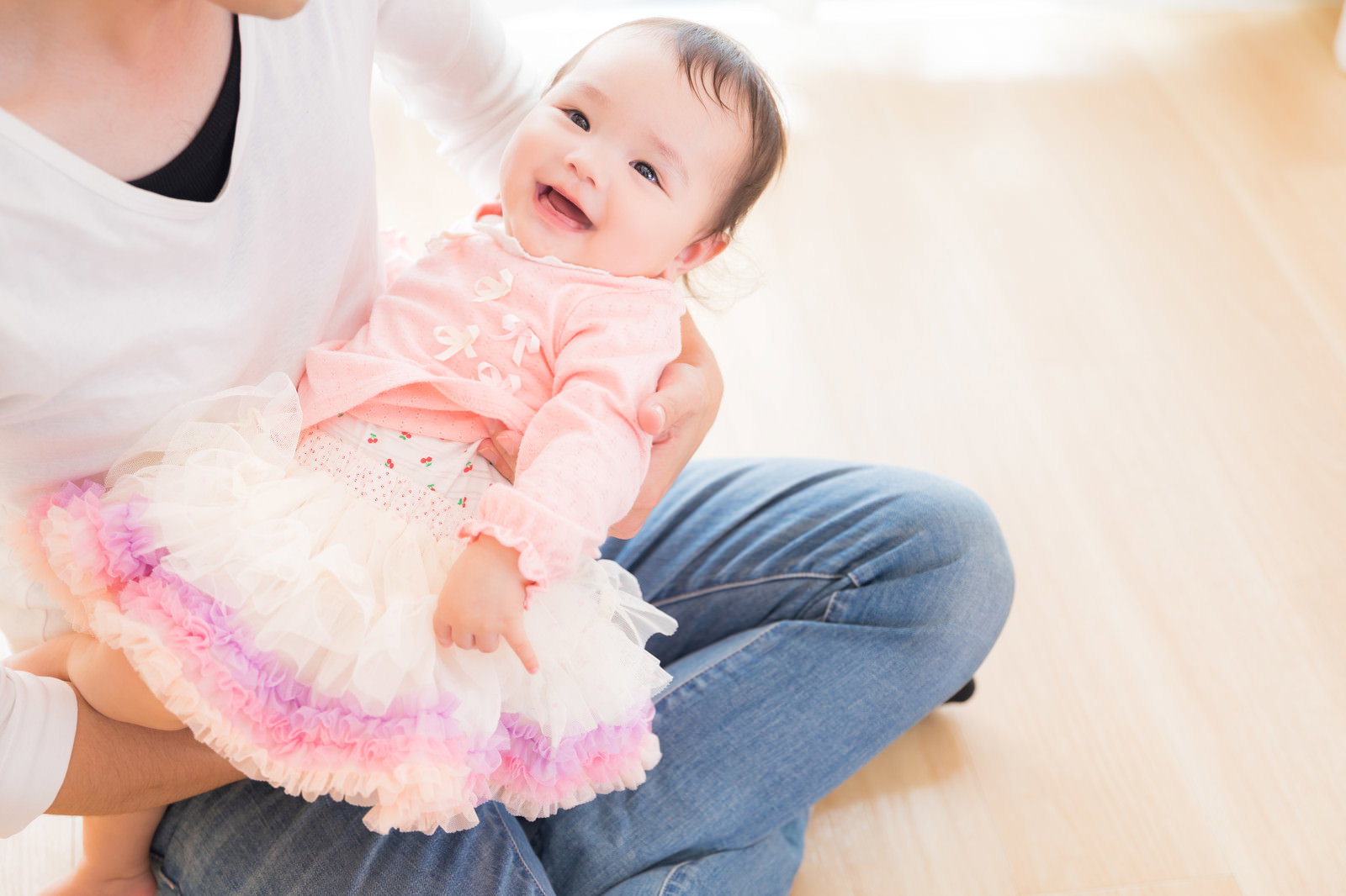 床に座って赤ちゃんをあやすパパの優しい表情と笑顔の親子［モデル：めぐな］