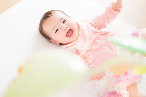 カラフルなベッドメリーを見上げて満面の笑みを浮かべる赤ちゃん