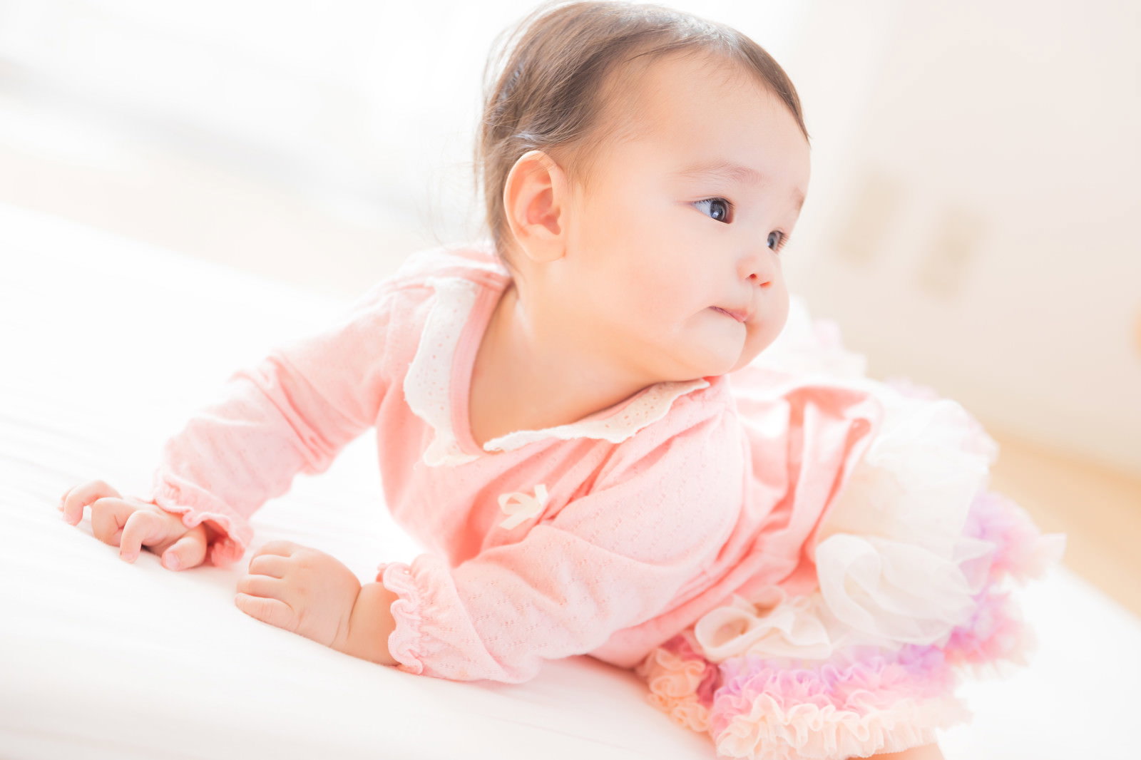 ピンクの服を着てにんまりと微笑む赤ちゃん［モデル：めぐな］