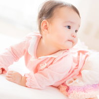 ピンクの服を着てにんまり微笑む赤ちゃんの笑顔の写真