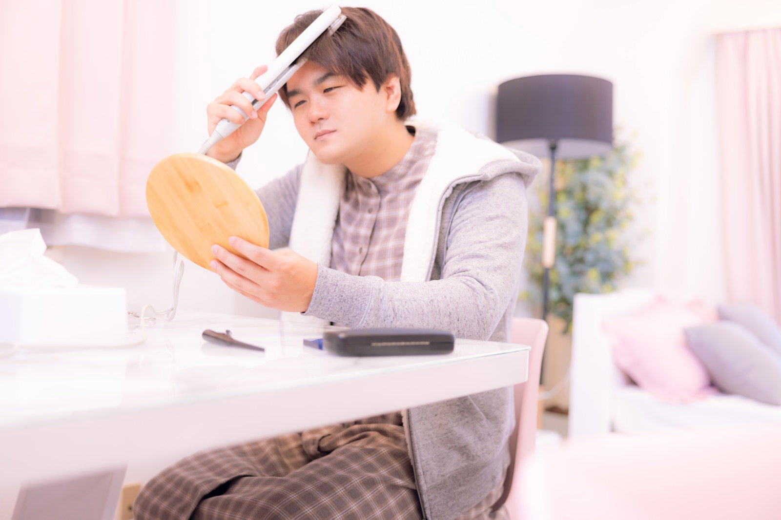 鏡の前でヘアアイロンを使って前髪をセットしている男性［モデル：はしも。］