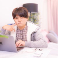 ノートパソコンの前で部屋着姿で悩む男性の頭を抱える姿の写真