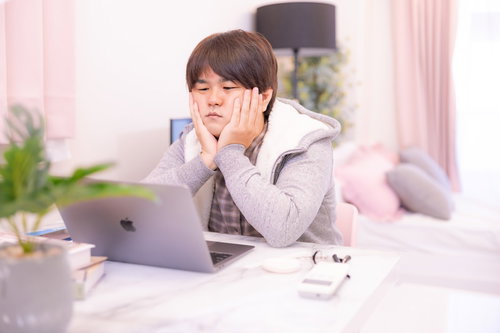 ノートパソコンの前で困惑する白いパーカー姿の男性