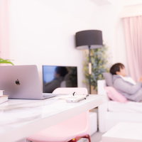 窓辺に横になる男性と卓上のノートパソコンの写真