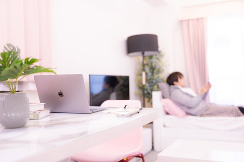 窓辺に横になる男性と卓上のノートパソコン