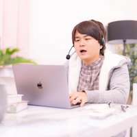 部屋着でヘッドセットをつけてオンライン会議に参加する男性の写真