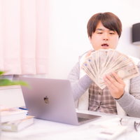 部屋着で一万円札を広げて札勘定の練習をする男性の写真