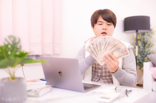 部屋着で一万円札を広げて札勘定の練習をする男性