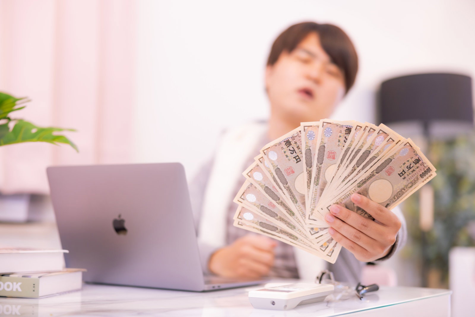 デスクで扇型に広げた一万円札を手に持つ男性［モデル：はしも。］