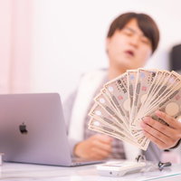 デスクで扇型に広げた壱萬円札を配信者に見せる男性の写真