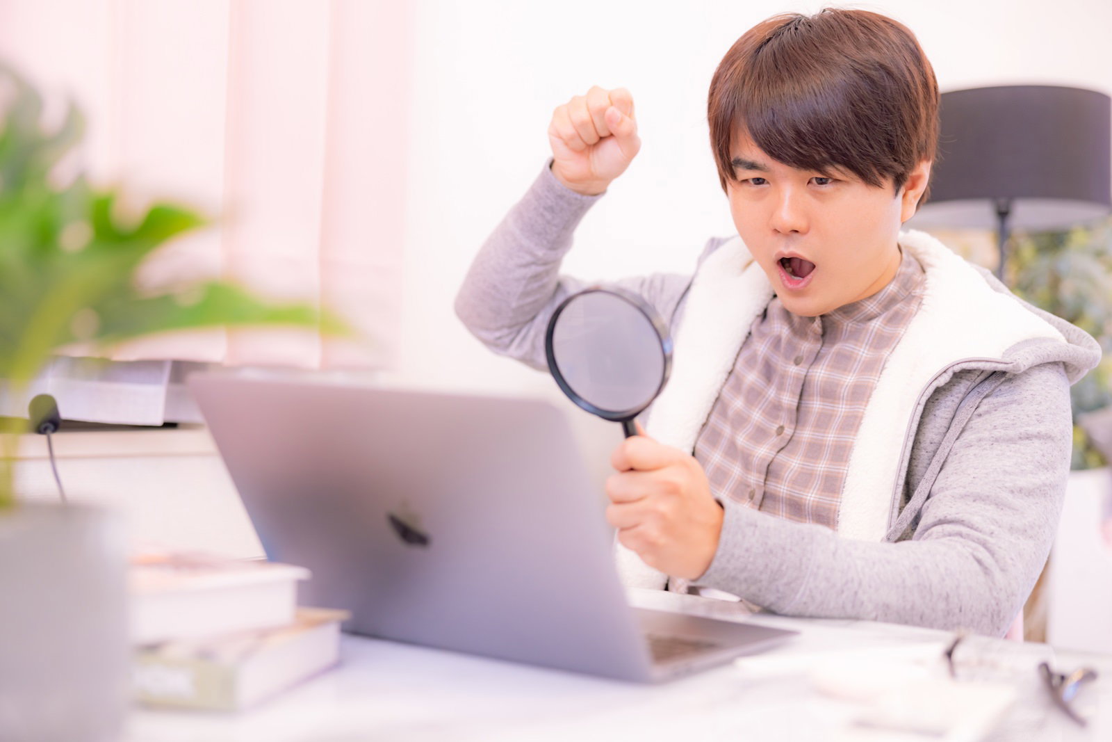 虫眼鏡を右手に持ちながらノートパソコンの画面を見る男性［モデル：はしも。］