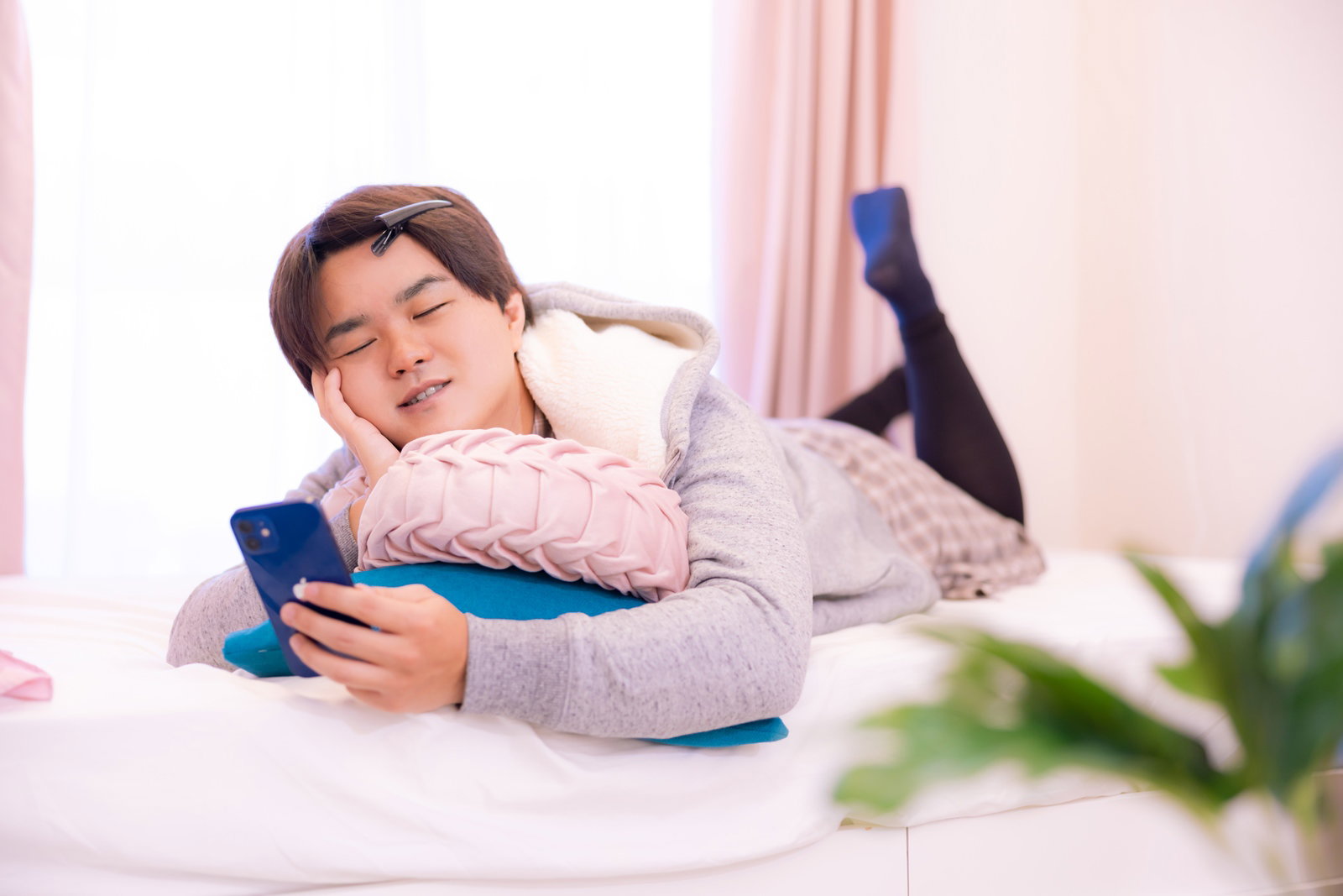 ベッドで横になり部屋着姿でスマートフォンを見る男性［モデル：はしも。］