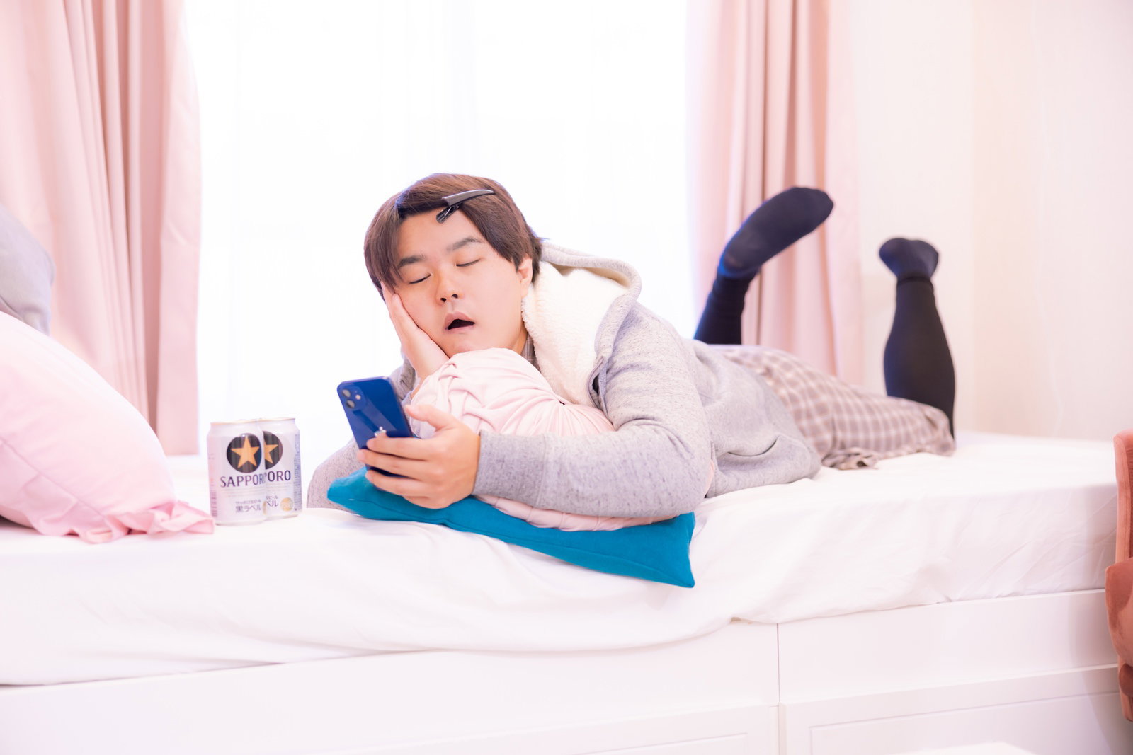 部屋着を着た男性がベッドに横になってお酒を飲みながらだらだらとくつろいでいる様子［モデル：はしも。］