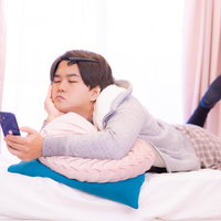 部屋着でベッドに横たわりスマホを見る男性の写真