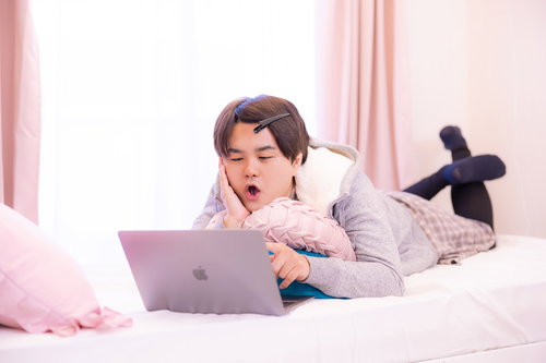 部屋着でベッドに横たわりネットサーフィンする男性