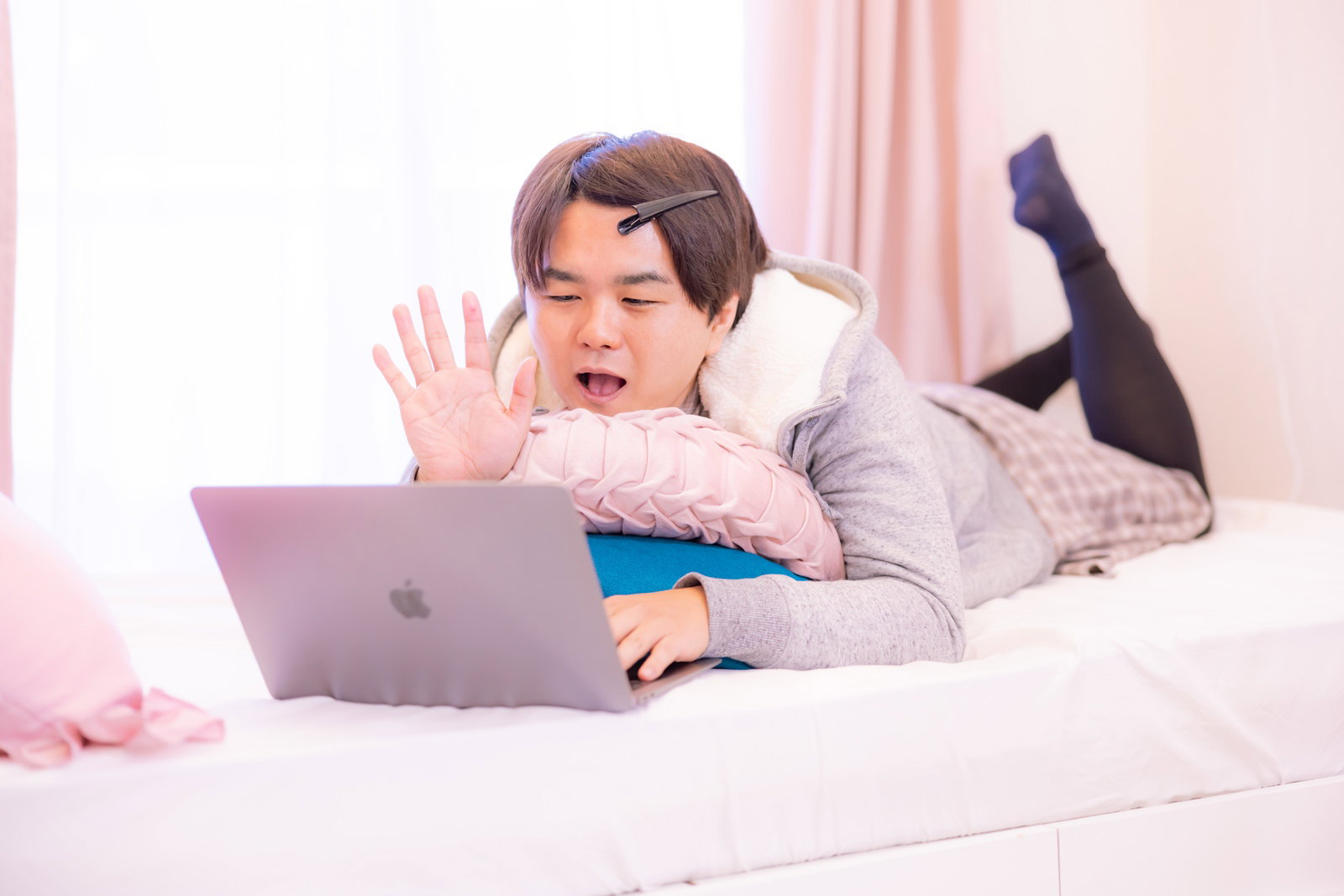 ベッドに寝転んでノートパソコンでZOOMをする白いシャツの男性［モデル：はしも。］