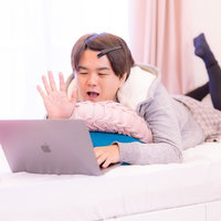 ベッドに寝転びながらZOOMで通話する男性の写真