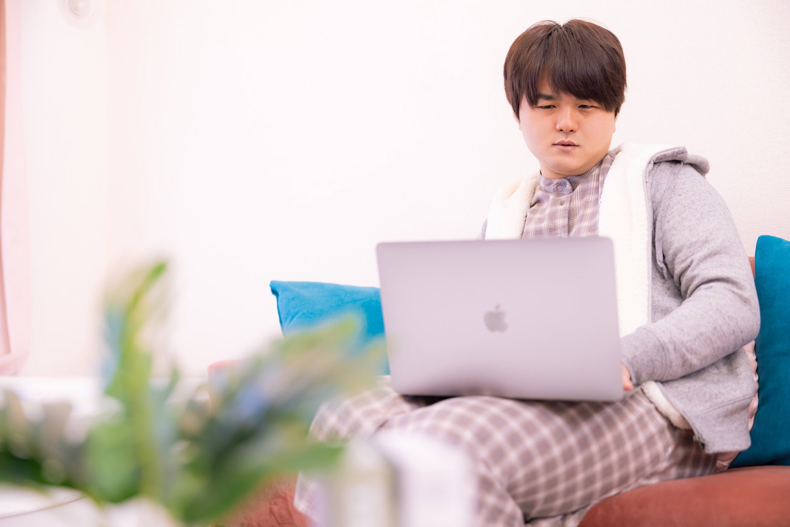 グレーの部屋着を着た男性が膝の上にノートパソコンを置いてネット検索している［モデル：はしも。］