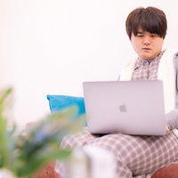 膝の上にノートパソコンを乗せてネット検索する男性の写真