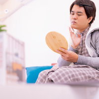 鏡を見て部屋でお化粧をする男性のメンズメイクの写真