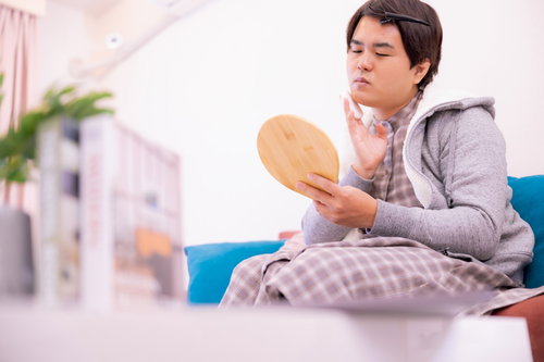 鏡を見て部屋でお化粧をする男性のメンズメイク