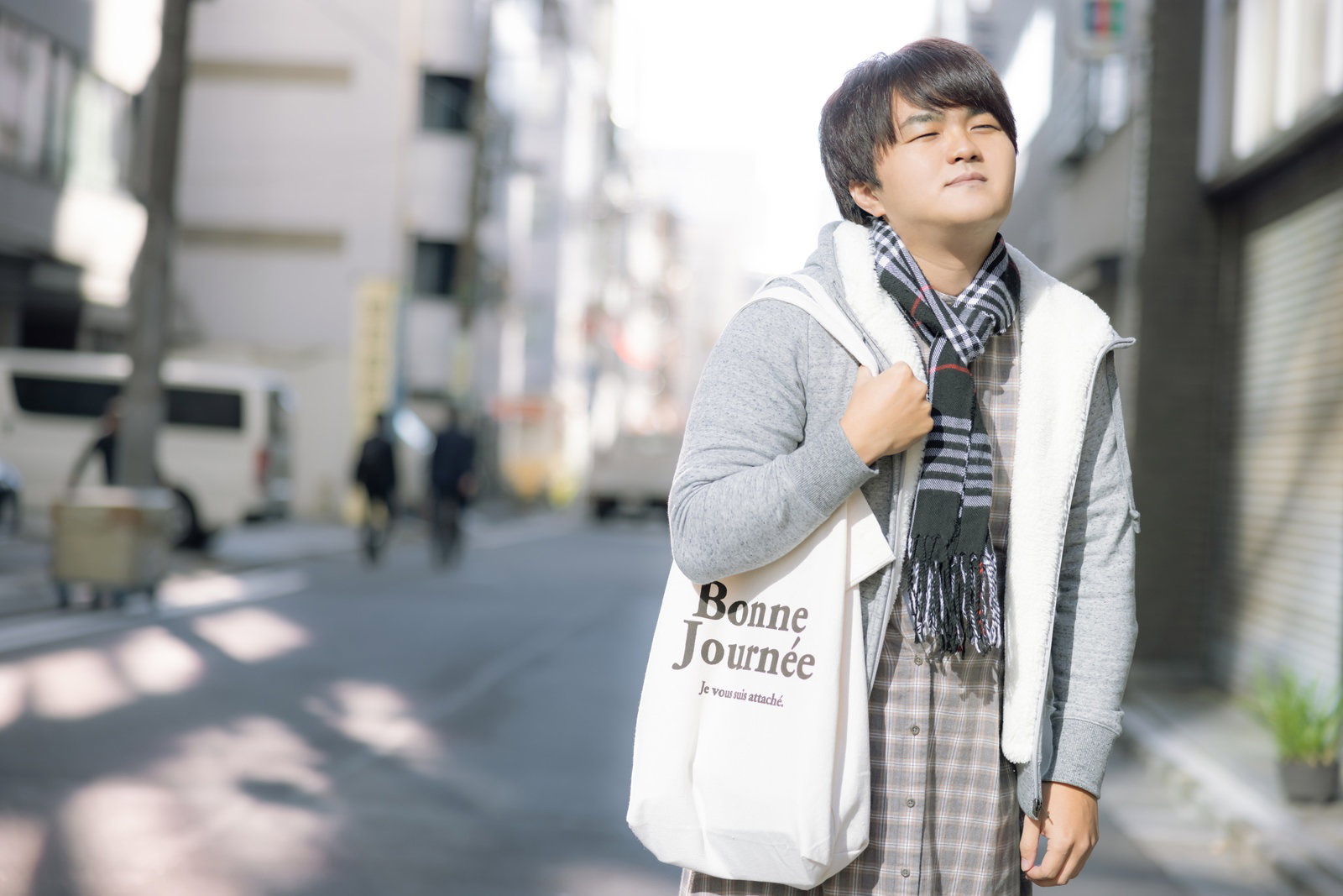 白いシャツにストライプのベストを着た男性が街中の歩道を歩いている［モデル：はしも。］