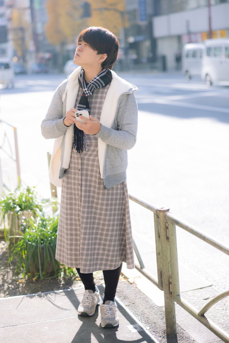 ベージュのコートを着た男性が街角で不安そうに上を見上げている［モデル：はしも。］