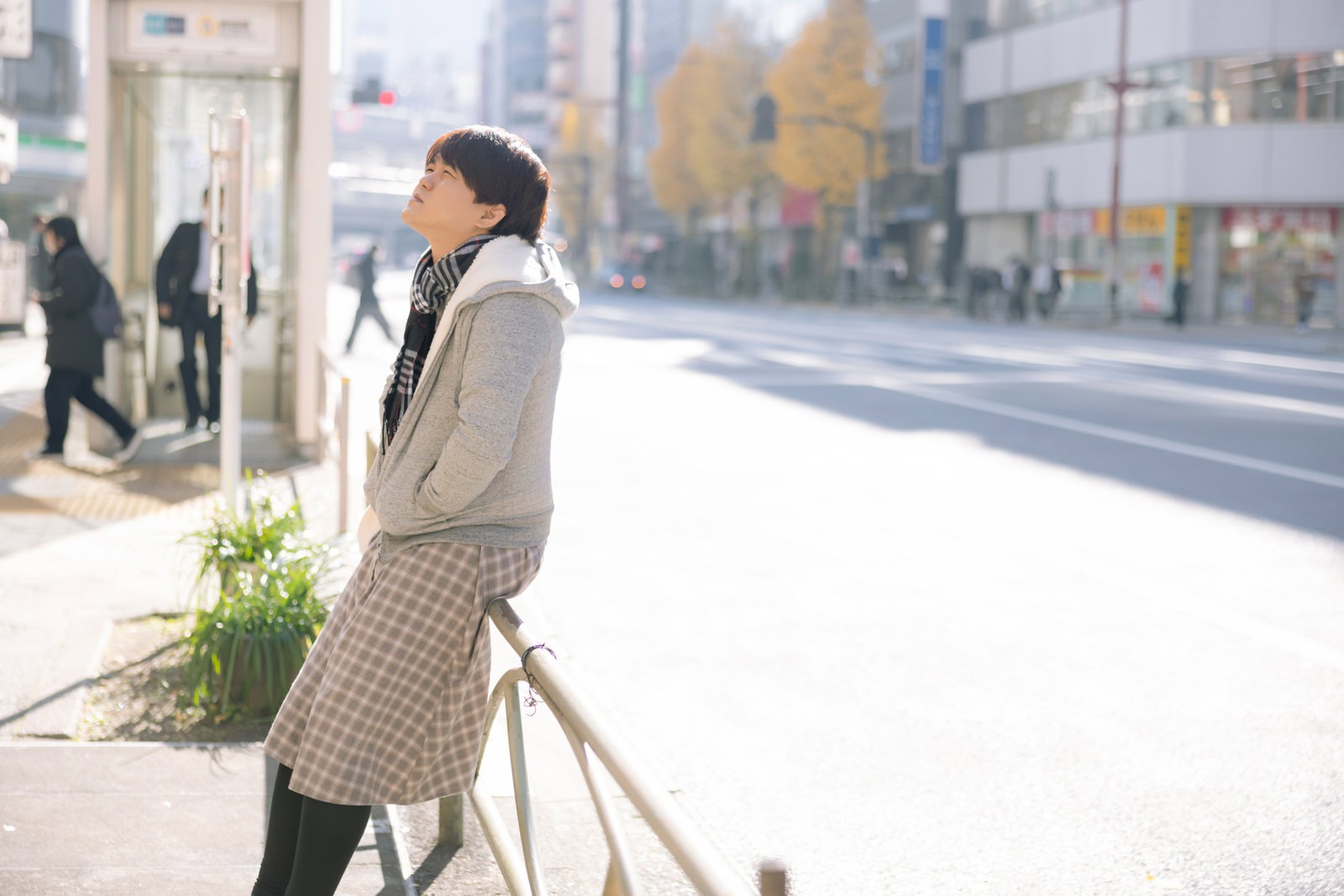 マスクを着用してベージュのコートを着た男性が花束を持って街中を歩いている様子［モデル：はしも。］