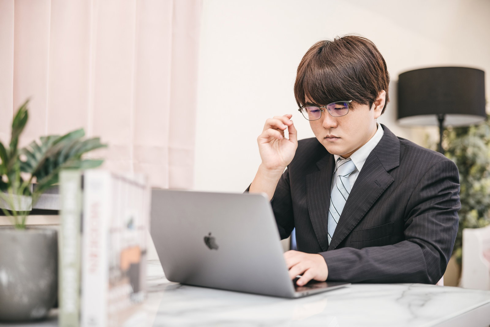ワークスペースでノートパソコンを操作するスーツ姿の男性会社員［モデル：はしも。］
